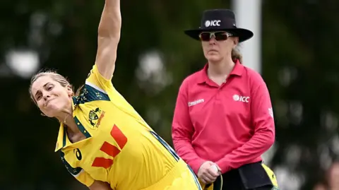 Sophie Molineux bowling as an umpire watches on