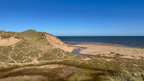 BBC Weather Watchers - Anne's World A grassy sand hill with the sea in the background and clear blue skies. 