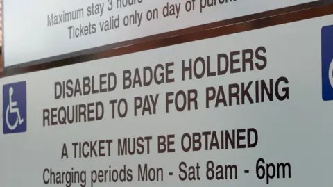 A sign instructing disabled badge holders that they must pay for parking and a ticket must be obtained.