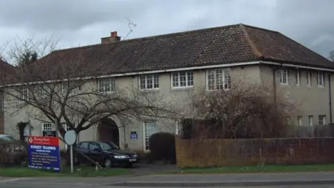 Malcolm Heathcote An exterior view of a brown building with multiple white windows.