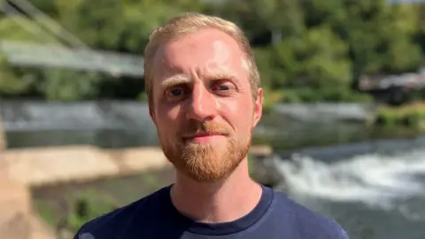 A man called Rob Willcocks. He appears to be in his late 20s or early to mid 30s and has short blonde hair. He also has a trimmed ginger beard.