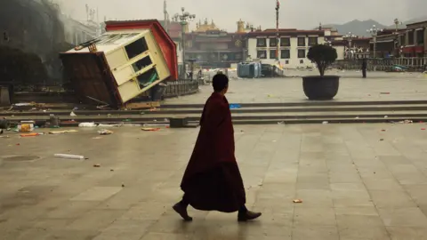 AFP via Getty Images A Tibetan monk walking past an overturned barrack at a square in Lhasa