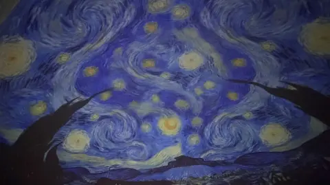 A projection of Vincent van Gogh’s “Starry Night” fills a curved planetarium dome, showing swirling blue skies, bright yellow stars and the dark silhouette of cypress trees in the foreground.