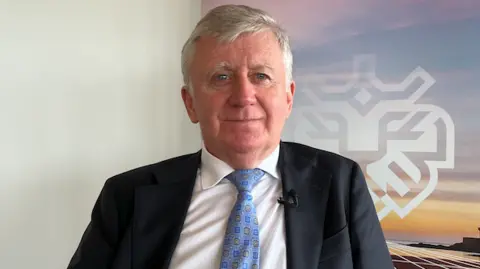 A man wearing a suit and blue tie with the Jersey Finance logo to his right behind him.