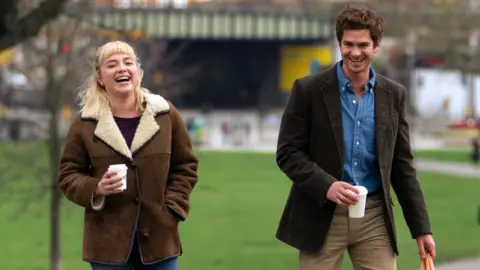 StudioCanal Florence Pugh and Andrew Garfield in We Live In Time seen walking through a park with takeaway coffee cups