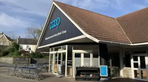 Coop store in Guernsey. Brown roof with trolley and blue Coop sign and white and black face of store