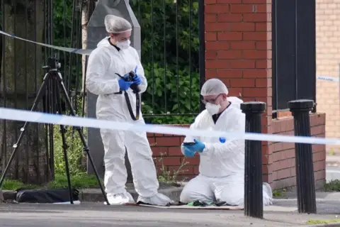 PA Media Forensic officers wearing white protective clothing and masks are picturing elements of the scene