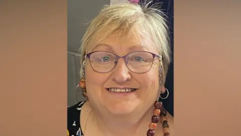 Vanessa Worrall Vanessa Worrall's face smiling and looking at the camera. She wears purple framed glasses. She has short blonde hair and blue eyes. She is wearing glasses and a chain of brown and orange beads and is also wearing silver hoop earrings.