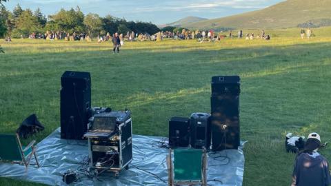 Photo of speakers and dozens of people gathered in the field at the stone circle.