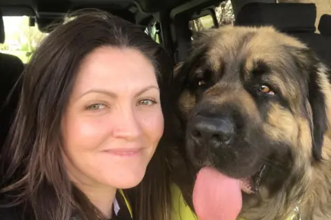 Supplied A close-up of a woman with brown hair, and a dog with a large face sticking its tongue out. They appear to be in a car or minivan.