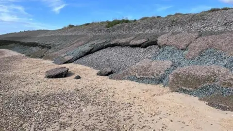 Tendring District Council Sloping sea defences bound with asphalt with sandy beach in foreground