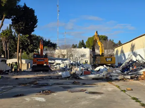 Israel Land Authority A yellow and a red excavator are situated among wreckage of demolished structures at the Unrwa compound in East Jerusalem (20/01/26)
