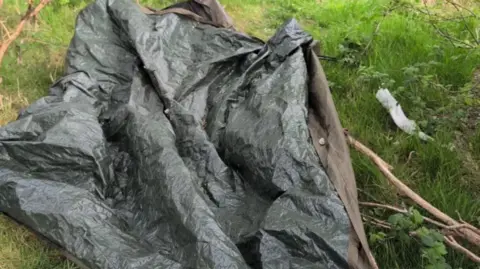 Cumberland Council A discarded tarp of a tent is covering greenery. There is also litter left nearby the branch.