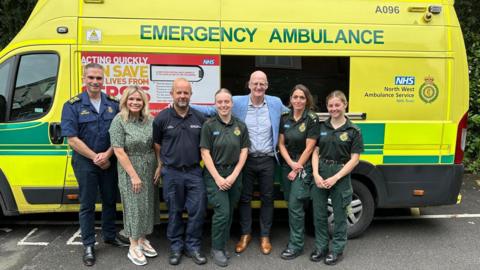 Iain Dowie (centre) with the team that saved him, standing in front of a North West Ambulance