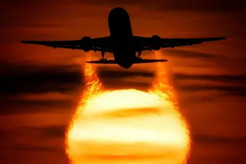 Solar photographer The sun in the sky casts an airplane in flight in silhouette. The sky is illuminated in orange with dark clouds streaking across it.