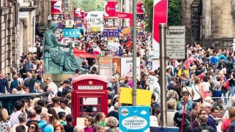 A massive crowd of people on a street among signs, statues and a red telephone box