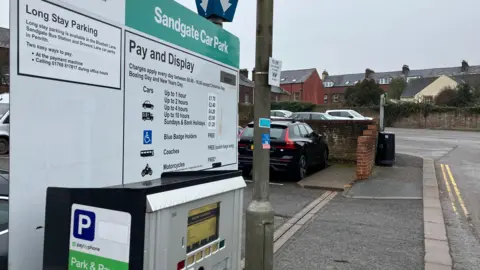 A pay-and-display sign at the entrance to Penrith's Sandgate car park. Cars are parked in the background.