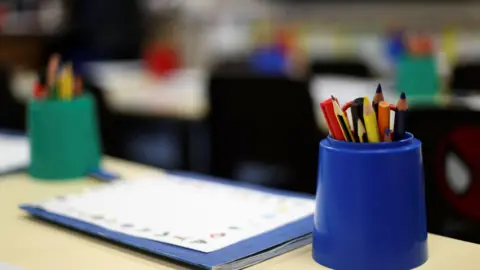 A blue plastic cup holding a variety of pencils in the foreground with a blurred out workbook and second plastic cup and pencils in the background