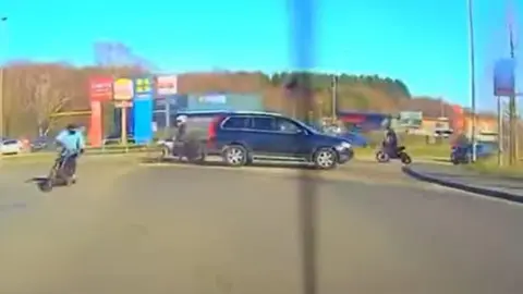 Supplied A still from dashcam footage showing a black car blocking a road on a roundabout and at least four people on bikes around it