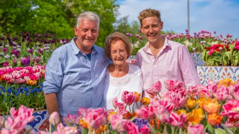 Tulleys Tulip Farm A group of two men and a woman stand in a colourful flower field. All three are looking at the camera.