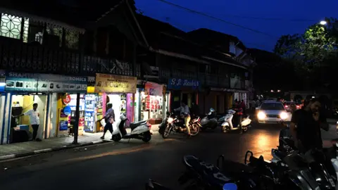 Getty Images Shops lit up in the evening along a street in the Goa District, India.