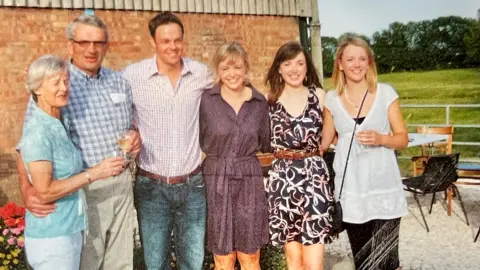 Michael Read Sheena and Michael Read stand with their four grown-up children in front of a red-brick wall in a farm yard. They wear summer clothes and a table and chairs can be seen to one side. In the background is a green paddock and trees.