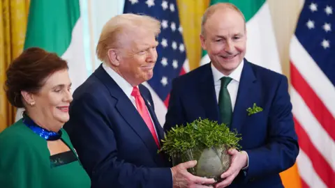 EPA-EFE/REX/Shutterstock The Taoiseach of Ireland Micheal Martin (R) and his wife Mary O'Shea (L) present US President Donald Trump with the traditional shamrock bowl during a St Patrick's Day reception at the White House in Washington DC