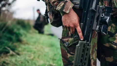 Getty Images Close up view of a solider holding an assault rifle on a military training exercise in a rural location.