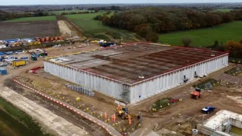 John Fairhall/BBC A drone image of the water storage reservoir and pumping station. A large square building is in the process of being built. Workers in orange hi-vis suits can be seen working around the site. Other building infrastructure can seen around the square building.