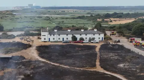 Reuters White coastguard cottages at Dunwich surrounded by charred black ground from the wildfire. Fire engines and cars are parked next to them.