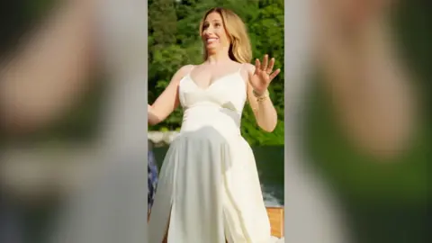Stacey Solomon wears a white dress while standing on a boat, with a forest in the background