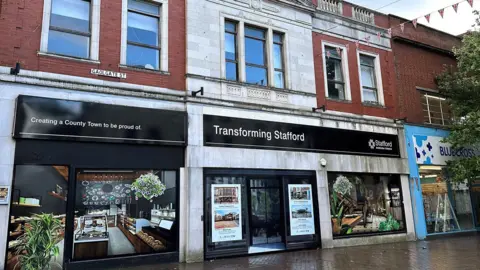 The front of a former high street shop in Stafford with black signage that says "transforming Stafford". 