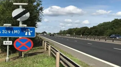 Dual carriageway with grass verge to the left and blue sign.