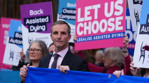 PA Media Lib Dem MSP Liam McArthur among demonstrators who support his bill. They are holding placards saying "Let us choose" and a blue banner.