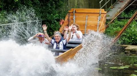 Wicksteed Park A modern day colour photo of the chute with four people in it at the bottom of the chute getting splashed as the chute hits the water.