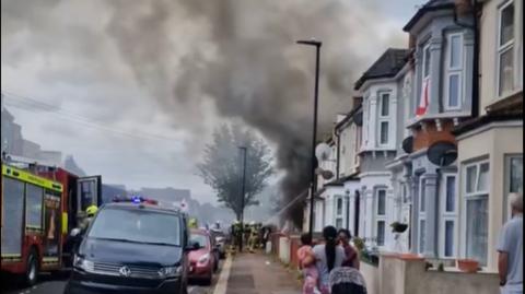 Image of smoke bellowing from the house as firefighters spray the blaze and onlookers watch on