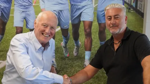 Barry Hearn, who is wearing a white shirt, shaking the hand of Jez Dickinson, who is wearing a black polo top.