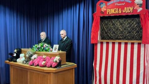 A Punch & Judy stand next to the coffin