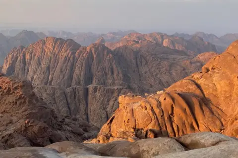 Ben Hoffler The mountains at dusk, from Jebel el Ahmar in 2024. Light hits the top of a rocky mountain range, which stretches into the distance 