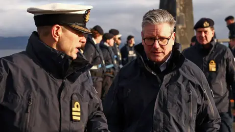 A member of the Royal Navy looks towards Sir Keir Starmer and speaks they walk along the top of a submarine, as he visits HMS Vanguard on Monday. There are other military personell in the background