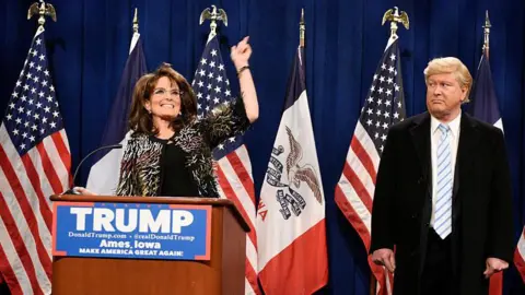 'AI can't write comedy', says Saturday Night Live star 5 NBCU Photobank Tina Fey stands at a lectern with a "Trump" sign on the front as she plays Sarah Palin, US flags i a row behind her. Darrell Hammond as Donald Trump is to her left, giving her the "side eye" look.