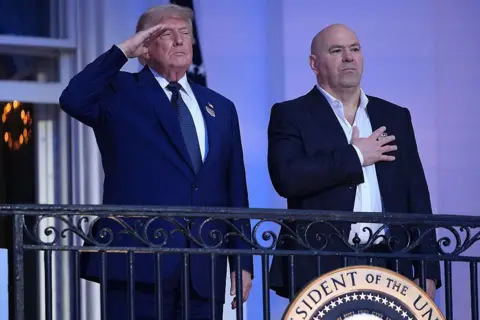 Getty Images US President Donald Trump gives a salute and UFC CEO Dana White puts his hand on his heart as they stand on the White House balcony during a UFC event
