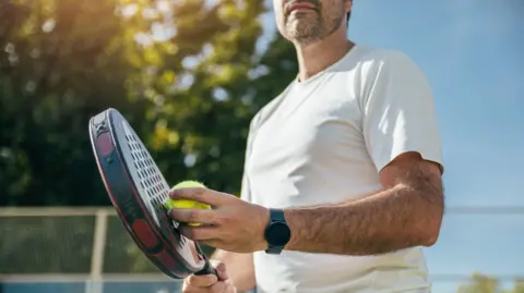 Getty Images Close-up of man holding padel racket and ball.