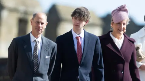 Getty Images Three people, a man, a woman and a young man, walk in smart clothes.