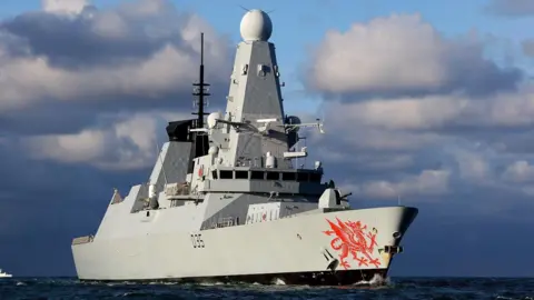 A warship is seen on the sea. It has a large red dragon painted on the front 