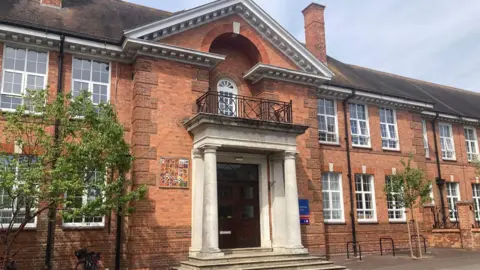 Front of one of the school buildings - a traditional large red brick building with pitched roof, large windows and a grand entrance with pillars