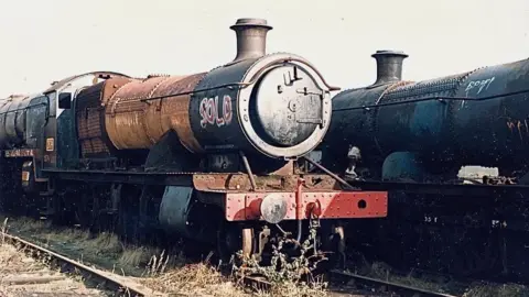 An old, rusty steam locomotive on old tracks with the word 'sold' spray-painted onto the side