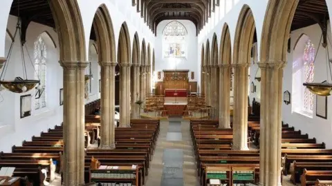 Inside St Mary's Church. Large columns line the main aisle of the church. Rows of seats sit either side of the room. An altar can be seen at the top of the aisle. 
