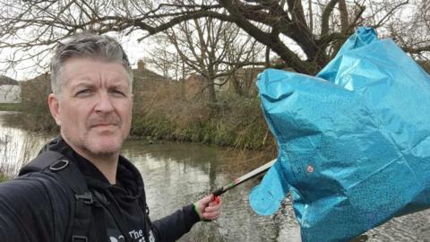 James Elliott holding up a blue star helium balloon with a river backdrop