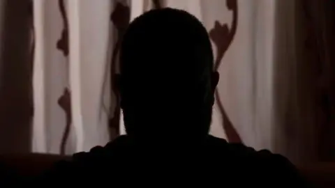 A picture taken from the BBC's anonymous interview with Ahmed, which is not his real name. He is seen in silhouette only, in front of a closed set of curtains in a dark room. 